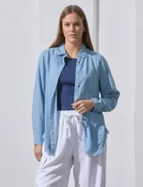 Camisa celeste de tencel con cuello, mangas largas, cierre frontal con botones, bolsillo en el pecho y ruedo con flecos.