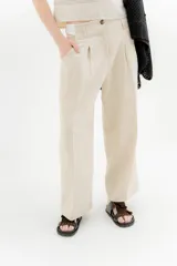 Pantalón de lino color beige, de tiro medio, corte ancho y pinzas frontales.