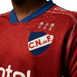 Camiseta de fútbol Umbro del Club Nacional de Football, modelo Away 1 2025. Diseño rojo con detalles en azul en cuello y mangas. Incluye logo de Umbro, escudo del club y sponsor Antel en el frente.