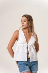 Blusa sin mangas color blanco, confeccionada en lino con detalles de broderie en la parte inferior. Presenta escote en V y cierre frontal con lazos.
