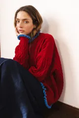 Sweater tejido rojo con cuello alto y puños con volados azules.