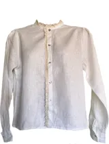 Camisa blanca de lino con cuello mao y puntilla de algodón en cuello y cartera de botones. Cierre frontal con botones de nácar y mangas largas con puños abotonados.