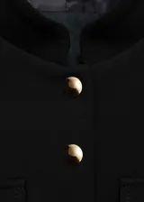 Chaqueta negra con cuello mao y cierre frontal con botones dorados. Tiene cuatro bolsillos de parche con solapa y botón.