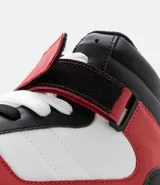 Championes de caña alta, color blanco, rojo y negro, con ajuste de cordones y velcro. Suela bicolor y puntera redondeada.
