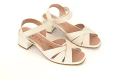 Sandalias de cuero color hueso, con tiras cruzadas en el empeine, talón descubierto y tobillera con hebilla. Taco cuadrado de 4 cm.