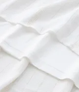 Vestido midi blanco confeccionado en tejido de viscosa con hilo metalizado, breteles finos de moña, escote v, busto marcado y volados en la pollera.