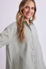 Camisa verde de corte holgado, con cuello clásico, cierre frontal con botones y mangas cortas con dobladillo.
