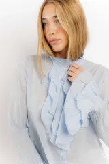 Camisa celeste de algodón con volados en el frente y mangas largas con volados en los puños.