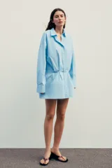 Vestido corto camisero celeste de algodón, con cuello solapa, manga larga con puños plisados, detalle de tablas en la falda y cierre frontal con botones.