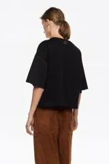 Camiseta negra de corte recto con escote redondo y mangas cortas anchas. Presenta pespuntes a contraste de color marrón claro en las sisas y los bordes de las mangas.
