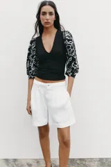 Top negro de escote pico con detalle de fornitura y mangas 3/4 abullonadas con estampado de flores bordadas.
