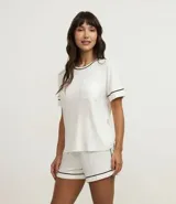 Conjunto de pijama de viscosa color blanco, compuesto por una remera de manga corta con bolsillo y un short con cintura elástica y bies negro en los bordes.