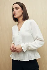 Camisa marrón de manga larga con escote en V y botones forrados al tono en el frente. Destaca por su textura sutil y por el detalle de frunces con volados en la parte inferior.