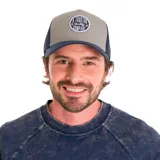 Gorro trucker con visera curva, paneles frontales grises, paneles traseros de malla azul marino y parche frontal con el logo de "Tractor Quality Company".