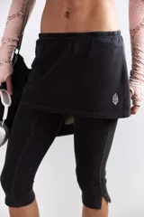 Calza deportiva cropped negra con una mini falda superpuesta de tiro alto y elástico. La calza presenta costuras deportivas y aberturas en los tobillos.