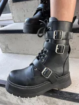 Bota de ecocuero negra con caña media, plataforma y hebillas decorativas.