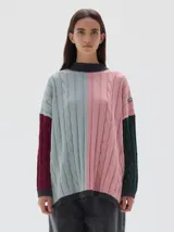 Buzo tejido colorblock con cuello subido tipo polera, diseño oversized y largo con pequeños cortes laterales. Presenta bloques de color rosa, celeste, bordó y verde oscuro, con cuello, puños y dobladillo en gris oscuro.