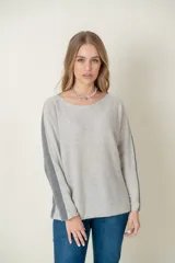Sweater de lana gris claro con mangas largas y corte holgado. Presenta una franja vertical gris oscuro a lo largo de cada manga.