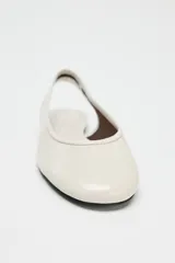 Zapato tipo bailarina destalonada en color crema, con detalle de pespunte en el corte, tira trasera con pieza elástica y acabado en punta redonda.