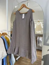 Vestido corto sin mangas, color beige claro, con cuello redondo y un volante o ruedo con volado en el bajo.