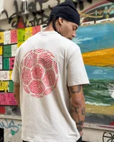 Remera color crema de corte clásico con cuello redondo y estampado en la espalda de una huella digital con forma de pelota de fútbol y el logo de Umbro.