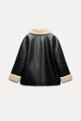 Cazadora negra de cuero sintético con interior de borreguillo color crema. Tiene cuello solapa, manga larga, bolsillos delanteros y cierre frontal con botones.