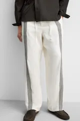 Pantalón relaxed fit confeccionado en tejido de lino color crudo. Cintura elástica ajustable con cordón, bolsillos laterales y traseros. Perneras con aplicación de bandas verticales negras a contraste en delantero.