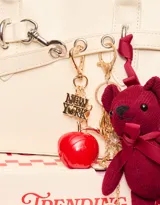 Llavero con dije de manzana roja, dije con la frase "New York" y dije de oso de peluche color borgoña con moño de cinta.