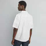Camisa blanca de manga corta con cuello clásico y cierre abotonado.