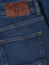 Pantalón de jean azul oscuro, corte recto, con cierre de botón y cremallera, cinco bolsillos y parche con logo de Tommy Hilfiger bordado en la parte trasera.