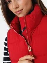 Chaleco rojo acolchado con cuello alto, cierre frontal con cremallera dorada y bolsillos laterales con cremallera dorada.