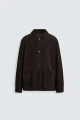 Sobrecamisa marrón de cuero gamuzado, corte recto, con cuello clásico, cierre frontal con botones, mangas largas con puños abotonados y bolsillos de parche en el pecho.