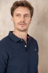 Chomba azul marino de piqué con cuello clásico, tapeta de dos botones y logo de pájaro bordado en color rosa en el pecho.