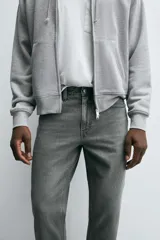 Jeans de denim de algodón, color negro lavado, con tiro medio, corte ajustado en cadera y muslos, y pierna que se estrecha hacia el tobillo. Presenta cinco bolsillos y cierre frontal con cremallera y botón.