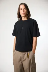 Remera negra de manga corta con cuello redondo y un pequeño estampado en el pecho de una cruz estilizada en color gris claro.