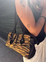 Cartera tipo baguette con estampado animal print blanco y negro, detalles en cuero negro y doble cierre superior.