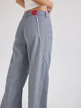 Pantalón largo de tiro medio alto a rayas verticales azules y blancas con costuras rojas a contratono. Presenta bolsillos delanteros y traseros, y cortes con desflecado.