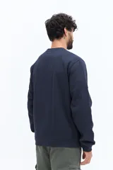 Buzo de algodón color marrón oscuro (ciruela/ciruela quemado) con cuello redondo, puños y ruedo acanalados. Presenta un pequeño bordado de motivos florales en el pecho.