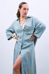 Vestido camisero largo celeste con bordado dorado de hojas, corte holgado, manga larga y cierre frontal con botones.