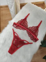 Conjunto de lencería de encaje rojo compuesto por un corpiño tipo bralette con tirantes finos y una tanga con tiras laterales ajustables. Ambas prendas presentan un diseño de encaje con motivos florales.