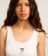 Musculosa de rib color blanco de la marca Blue Steel, con escote redondo ribeteado en encaje y detalle de moña negra bordada en el centro del pecho.