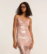 Vestido midi de malla con lentejuelas plateadas, escote recto y tirantes finos cruzados en la espalda. Presenta un forro corto que deja ver la transparencia de la malla con lentejuelas en la parte inferior, creando un bajo asimétrico.