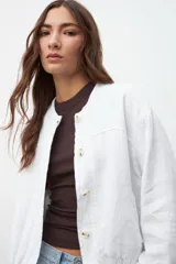 Chaqueta bomber blanca de lino con cuello redondo, cierre frontal con botones y mangas largas.