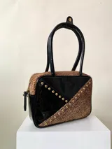 Cartera rígida negra de cuero con tachas plateadas y tres combinaciones de cuero diferentes que aportan textura. Tiene herrajes y cierre metálico plateado marca YKK. Cuenta con un asa fina para llevar al hombro o en la mano y una correa larga extra regulable.