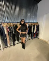 Top negro con escote halter que se ata en la nuca y la espalda, con detalle de nudo en la parte baja de la espalda. La prenda tiene un tejido con textura de terciopelo o jacquard con diseño de arabescos.