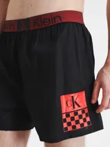 Short de baño negro con cintura elástica roja con logo Calvin Klein y estampado de tablero de ajedrez con logo CK en la pierna.
