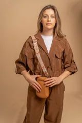 Bandolera pequeña tipo 'phone bag' de símil cuero color rosado pálido, con cierre de cremallera y correa ancha de tela con diseño de chevron en tonos claros.