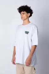 Remera blanca de corte oversize con mangas cortas y cuello redondo. Estampado pequeño en el frente con letras verdes.