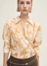 Camisa de manga larga color beige con estampado floral, cuello camisero y cierre frontal con botones.