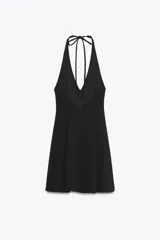 Vestido corto negro con cuello halter y lazada. Tiene bolsillos laterales ocultos y forro interior combinado. El cierre es en la espalda con cremallera oculta.